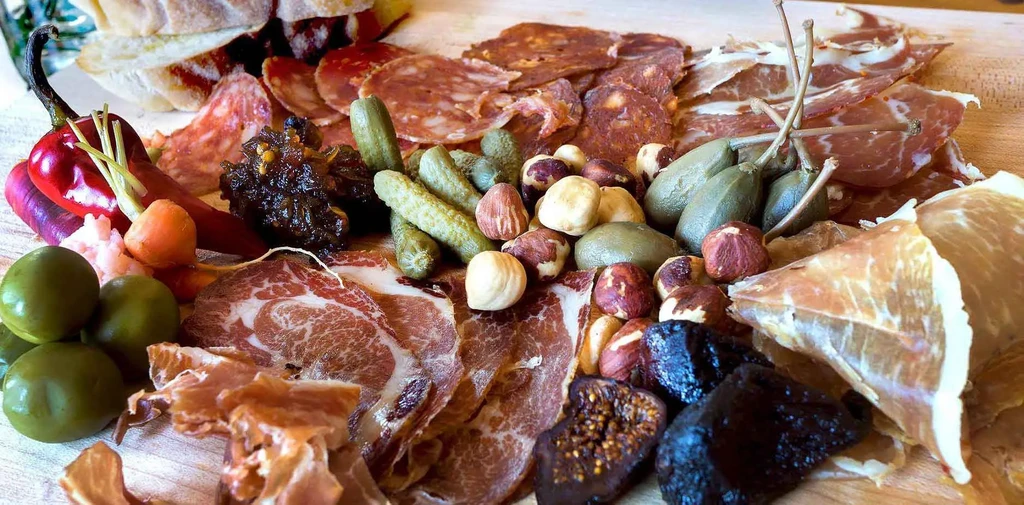 High-angle close-up of a charcuterie board with meats, olives, and peppers.