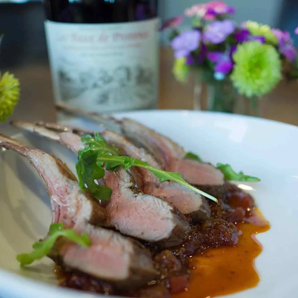 Lamb chops with sauce and greens on a white plate.