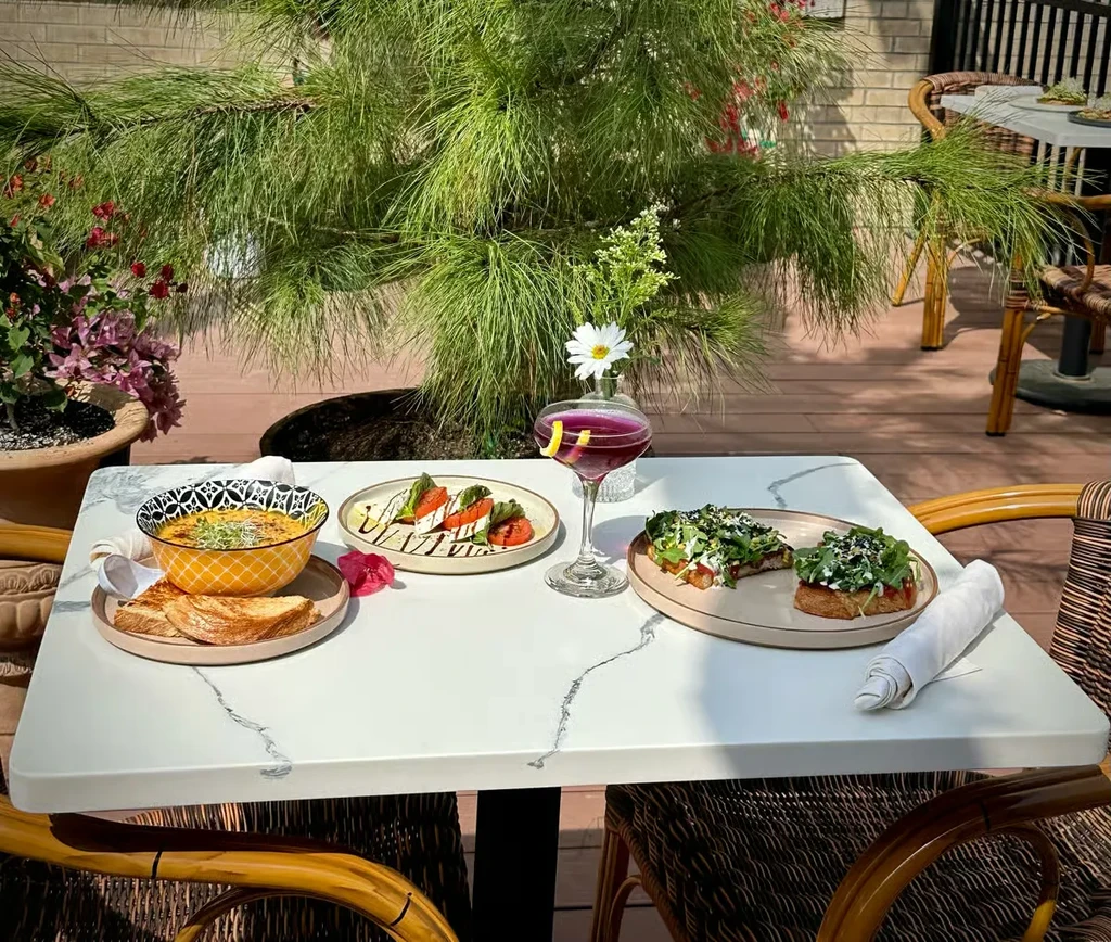 Outdoor dining table with soup, Caprese salad, cocktail, and toast.