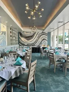 Empty restaurant dining room with set tables and a modern chandelier.
