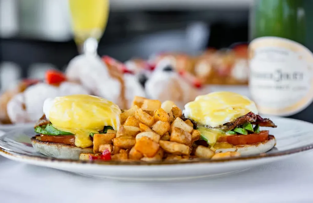 Two servings of Eggs Benedict with potato hash on a white plate.