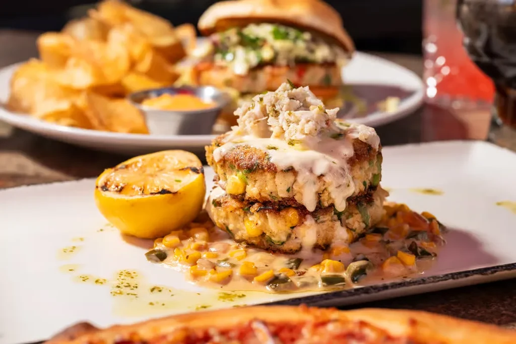 Close-up of crab cakes, corn, and grilled lemon on a table.