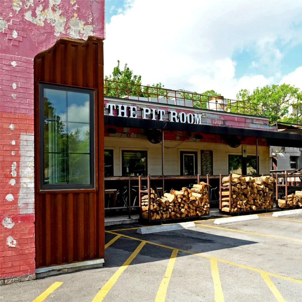 Exterior of The Pit Room restaurant with firewood stacks.