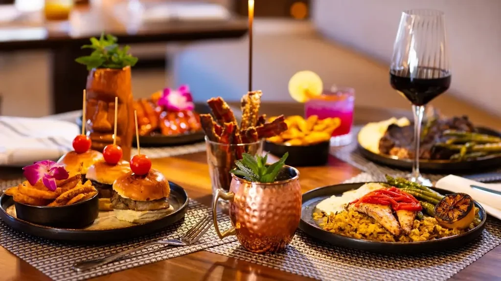 Restaurant table laden with diverse dishes and drinks, including sliders and fish.