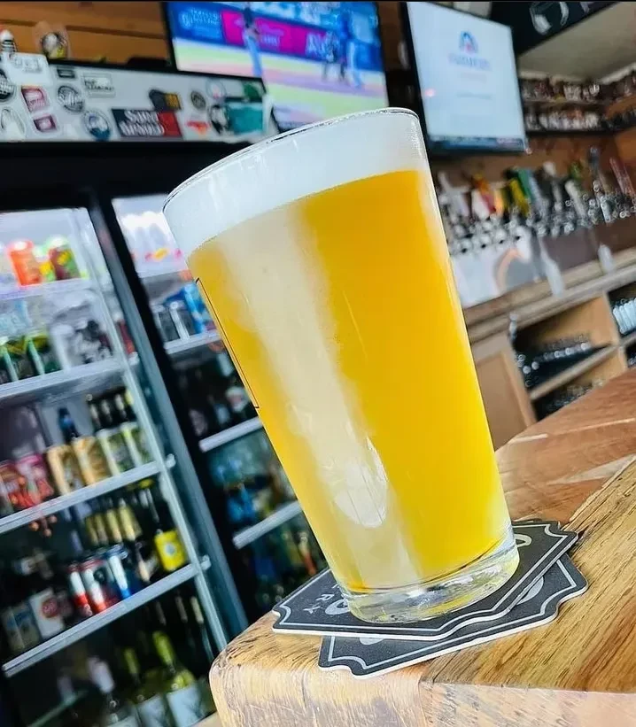 Full glass of beer with a frothy head on a wooden bar.