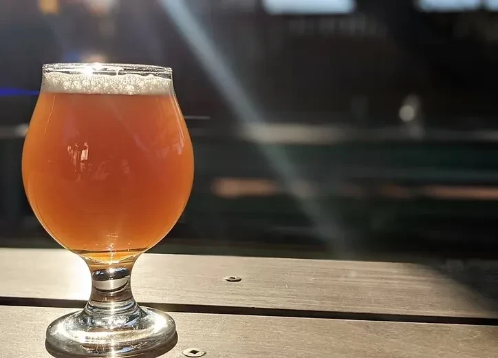Stemmed glass of amber beer with foam on a wooden surface.