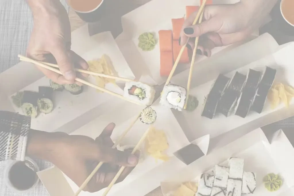 Overhead view of multiple hands picking sushi from takeout boxes.