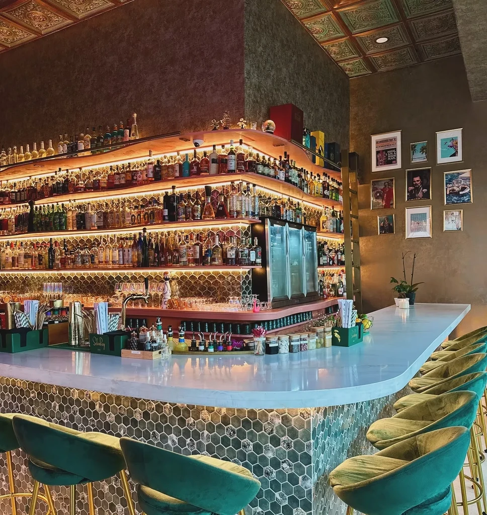 Bar counter with green hexagonal tiles, shelves of liquor, velvet stools.
