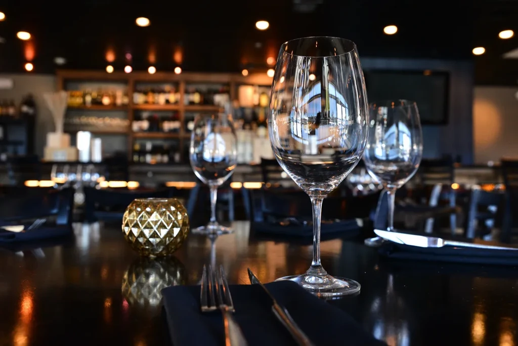Two wine glasses, silverware, and a votive on a dark table.