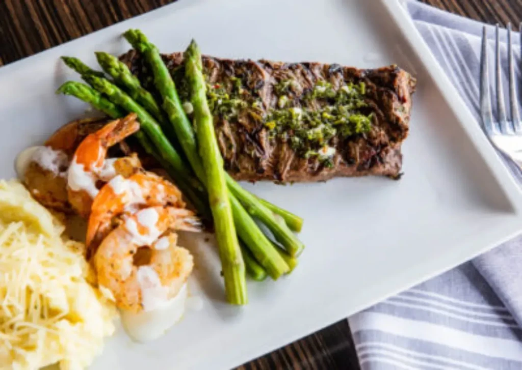 A well-plated meal of steak, asparagus, shrimp, and mashed potatoes.