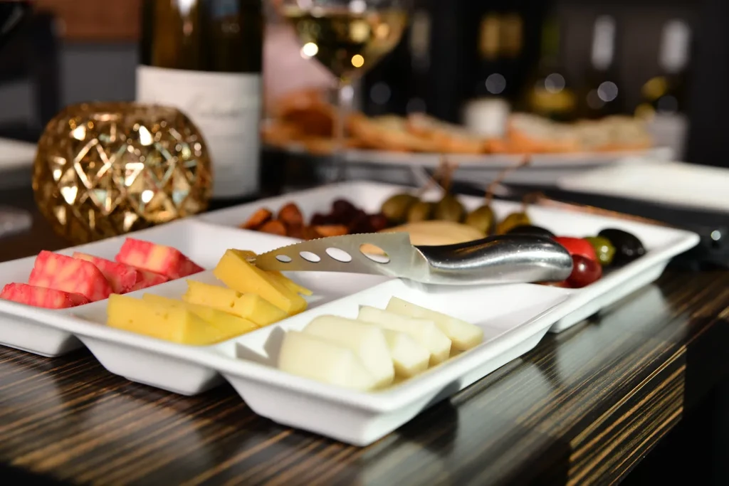 White rectangular platter with cheese slices, olives, nuts, and a cheese knife.