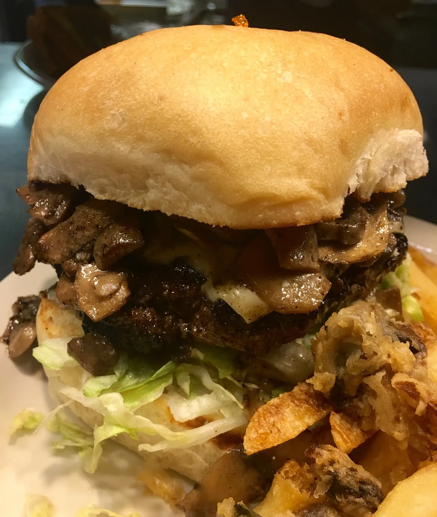 Close-up of a burger with mushrooms, cheese, lettuce, and fries.