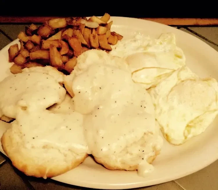 Plate of biscuits and gravy, fried eggs, and home fries.