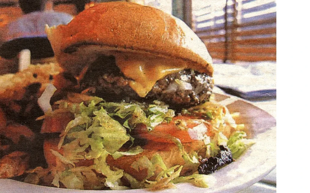 Close-up of a burger with melted cheese, lettuce, and tomatoes.
