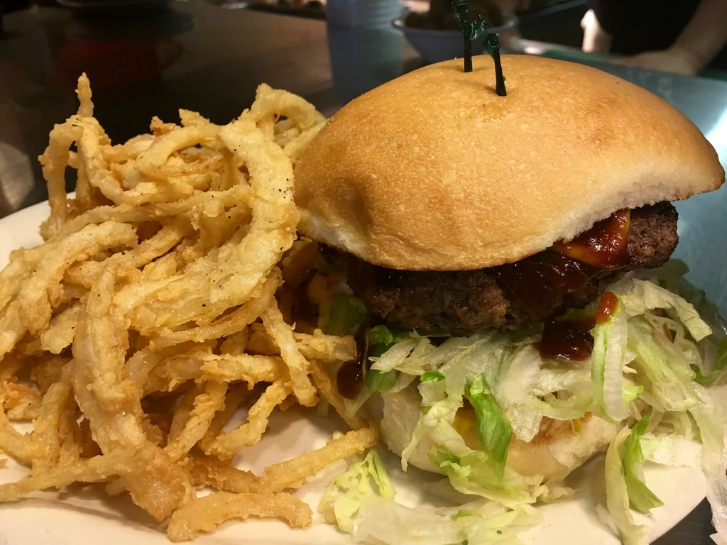 Close-up of a burger with onion rings on a white plate.