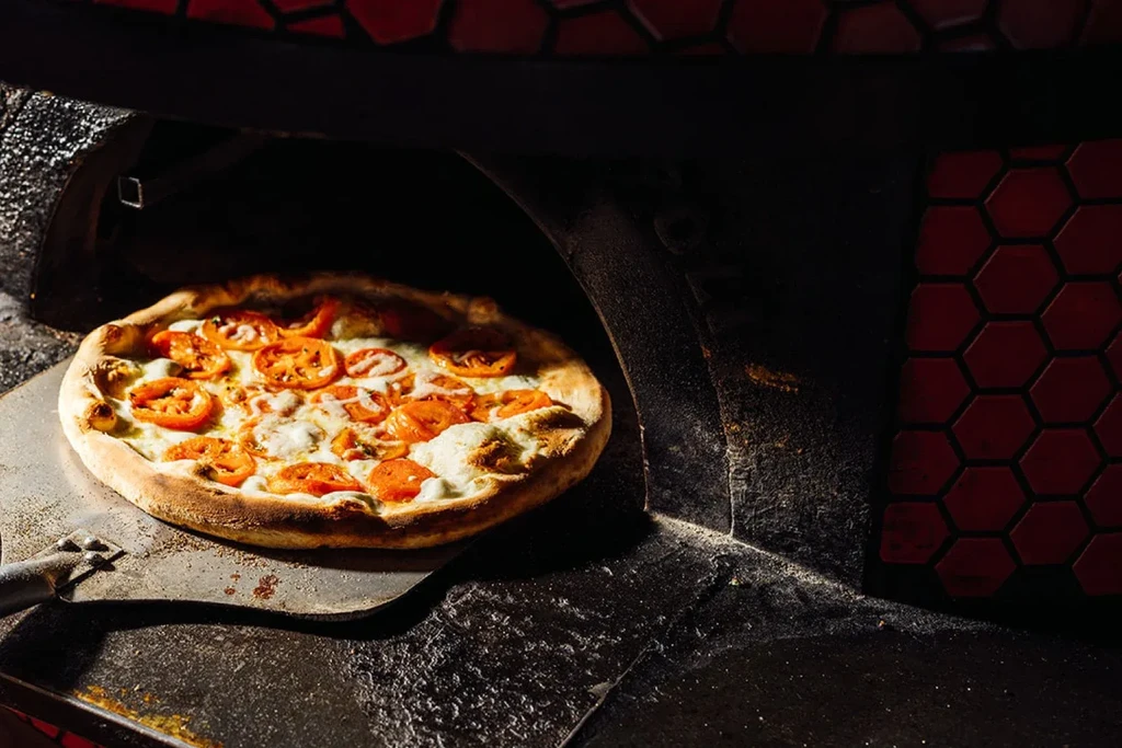 Pizza with cheese and tomatoes being removed from a brick oven.