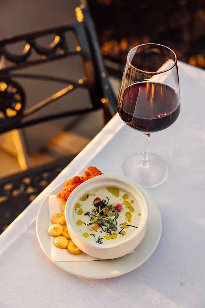 White bowl of creamy food with crackers, fried food, and red wine.