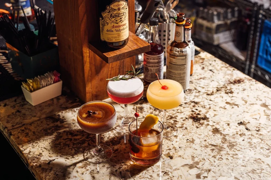 Four cocktails on a bar, garnished with coffee beans, berries, lemon.