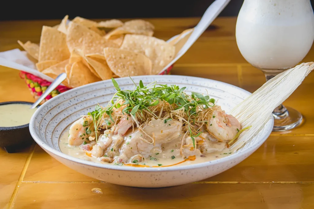 Creamy seafood dish with microgreens, tortilla chips, and a drink.