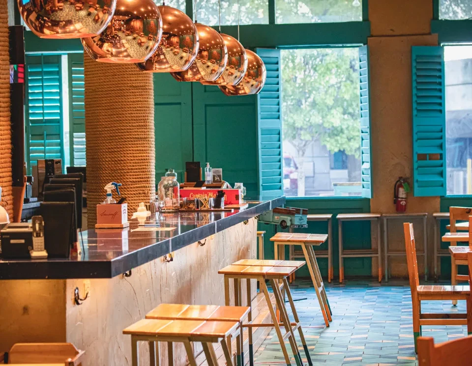 Interior of a restaurant with a bar, teal walls, and patterned floor.