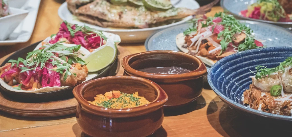 Variety of dishes, including tacos, on a wooden restaurant table.