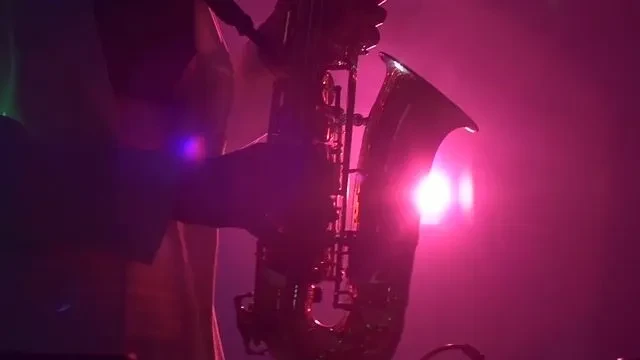 Musician playing saxophone under bright pink and purple stage lights.
