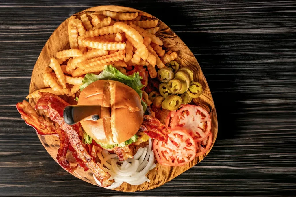 Gourmet burger, crinkle-cut fries, bacon, and vegetables on a board.
