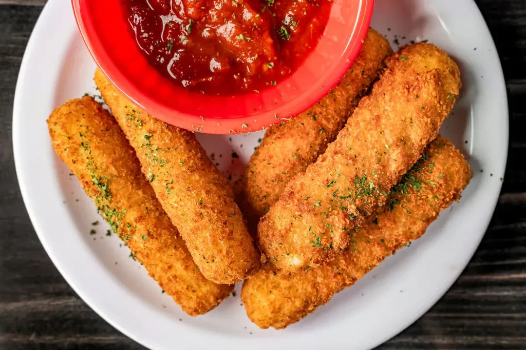 Fried mozzarella sticks with marinara sauce on a wooden table.