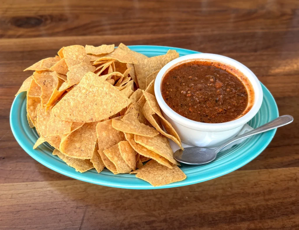 Teal plate of tortilla chips and salsa on a wooden table.