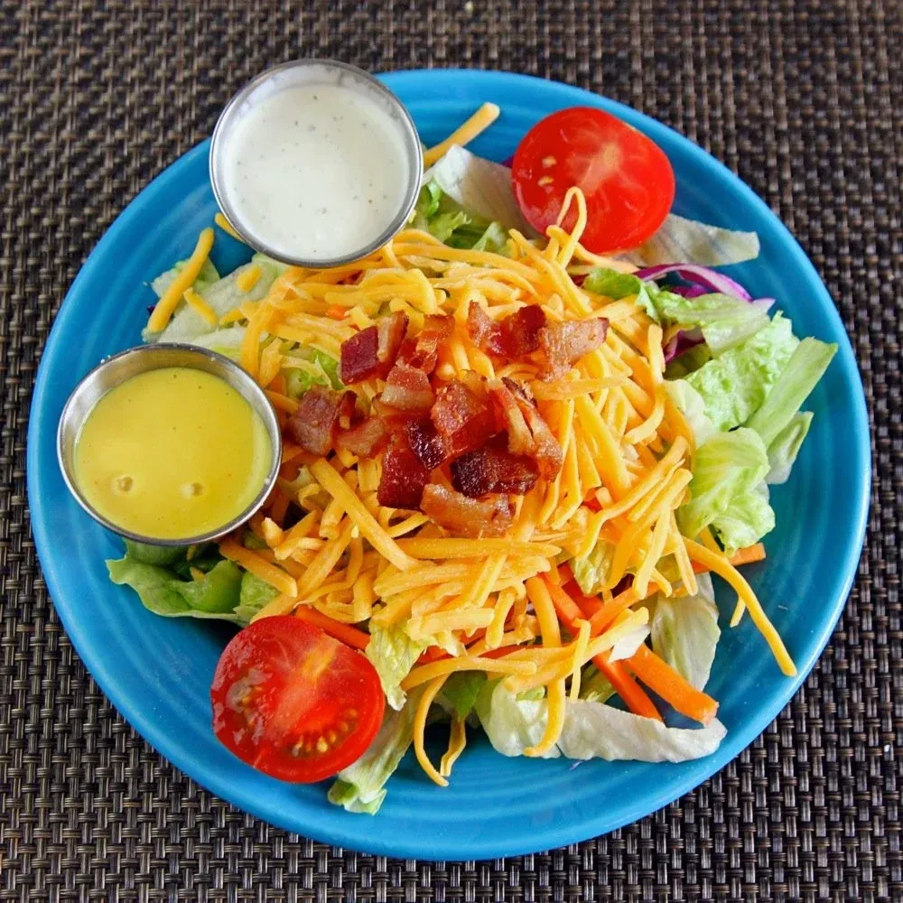 Overhead view of salad with lettuce, cheese, bacon, tomatoes, and dressings.
