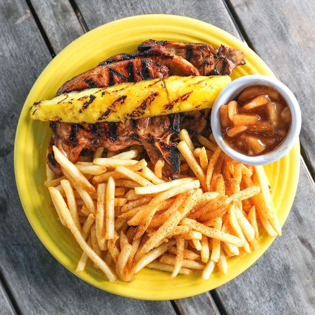 Grilled pork chop with pineapple, fries, and sauce on a yellow plate.