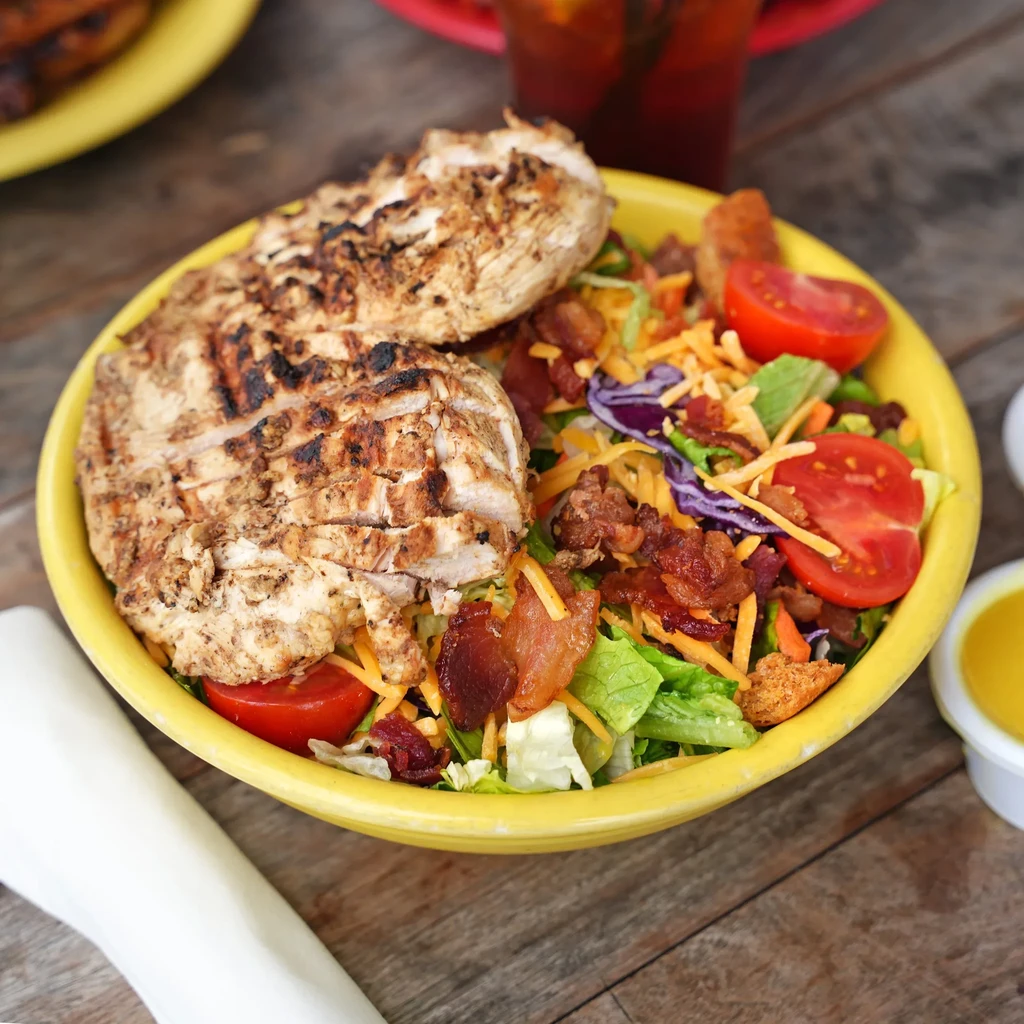 Grilled chicken salad in a yellow bowl on a wooden table.