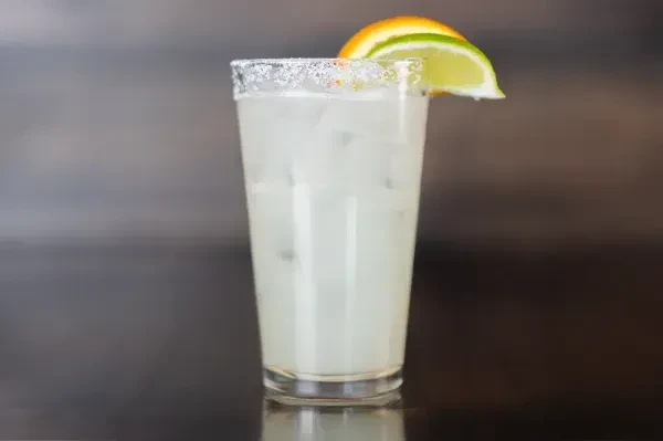 Glass of light-colored drink over ice with orange and lime.