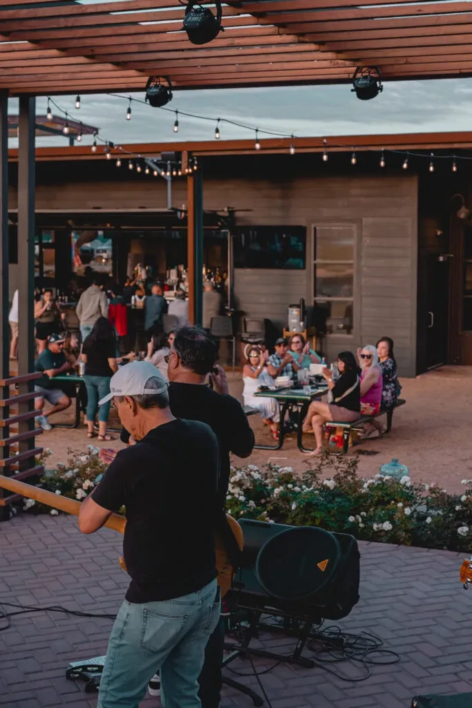 Two men play music for people gathered at an outdoor restaurant.