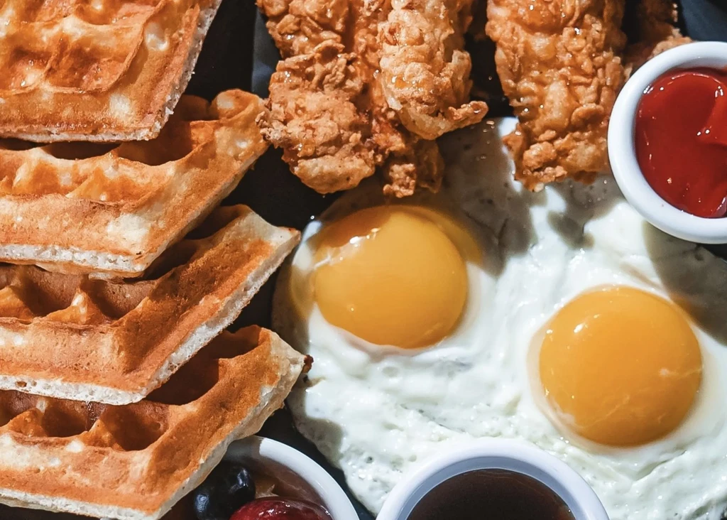 Waffles, fried chicken, and sunny-side-up eggs on a dark plate.