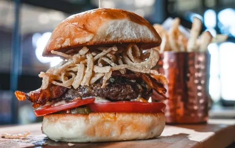 A burger on a brioche bun with beef, bacon, and fried onions.