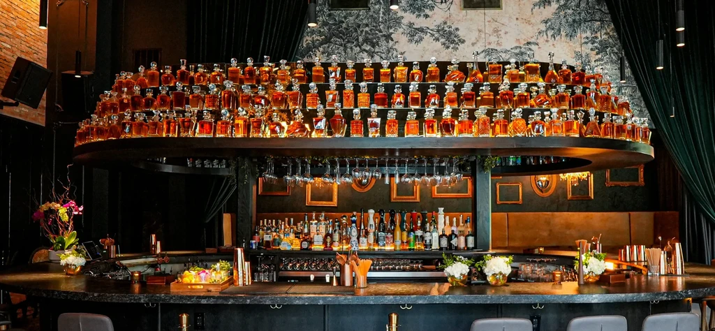 Luxurious bar with circular counter, tiered bottle display, and scenic wallpaper.
