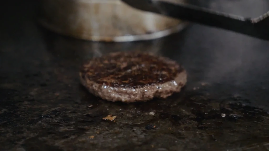 Hamburger patty sizzling on a well-used flat-top grill.