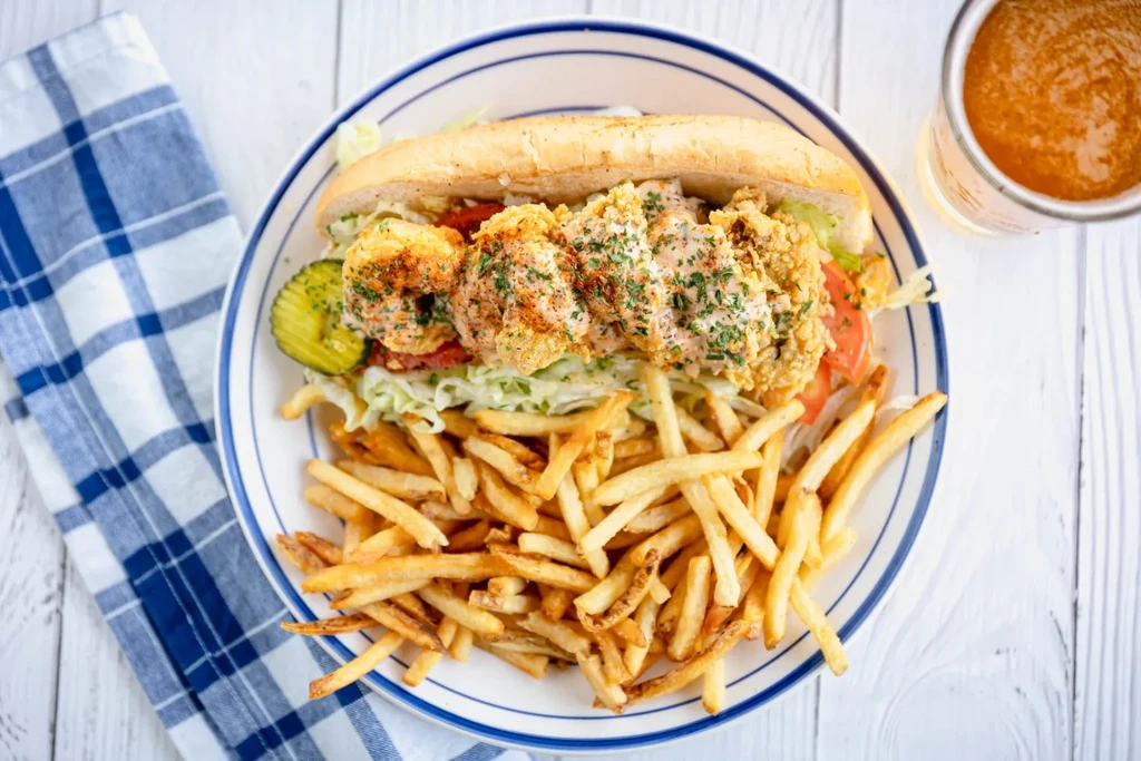 Shrimp po'boy sandwich with french fries, tomatoes, lettuce, and pickles.