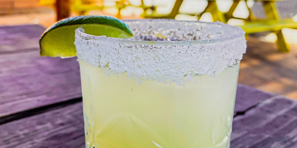 Margarita with salted rim and lime wedge on a wooden table.