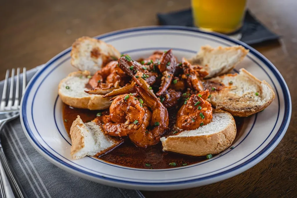 Plate of shrimp and crab claws in sauce with toasted bread.