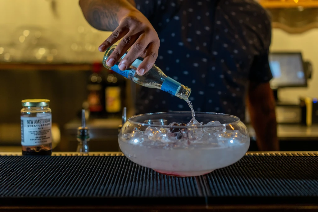 Bartender pours gin into a glass bowl with ice and berries.