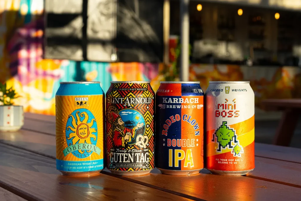 Four cold, colorful beer cans on a wooden table outdoors.