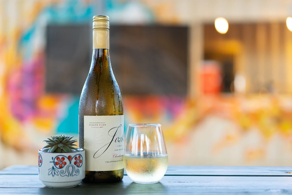 Josh Chardonnay bottle, wine glass, and succulent on a wooden surface.