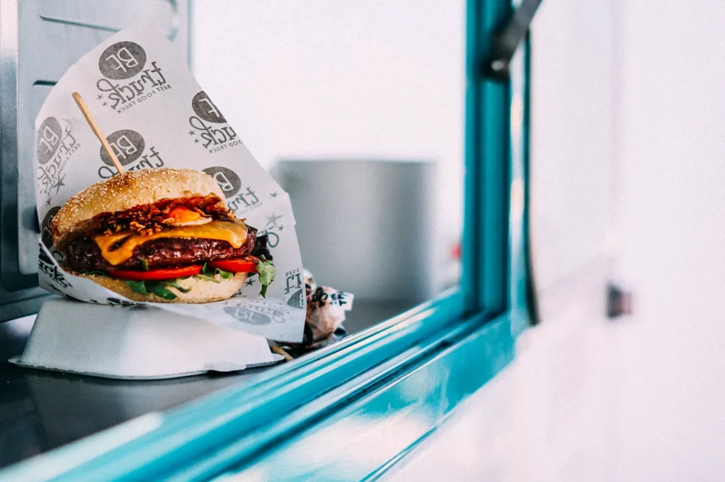 Gourmet burger in "Best Food Truck" wrapper on a steel counter.