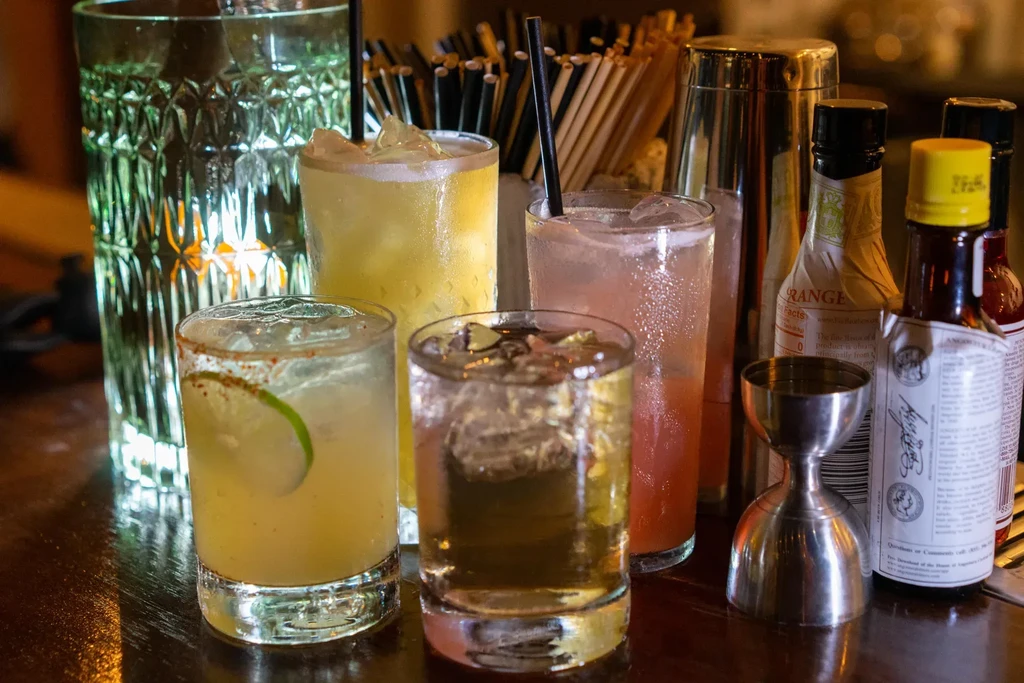 Five cocktails and bar tools on a polished wooden counter.