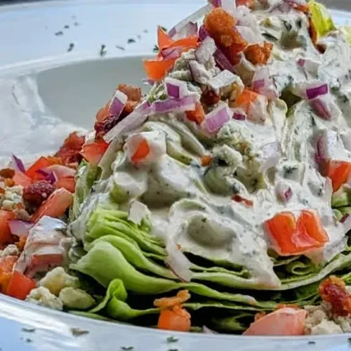 Close-up of a wedge salad with dressing, tomatoes, onions, bacon.