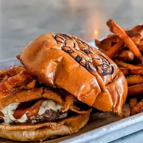 Gourmet burger with sweet potato fries on a metallic tray.