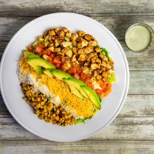Overhead view of a colorful salad with chicken, avocado, and cheese.