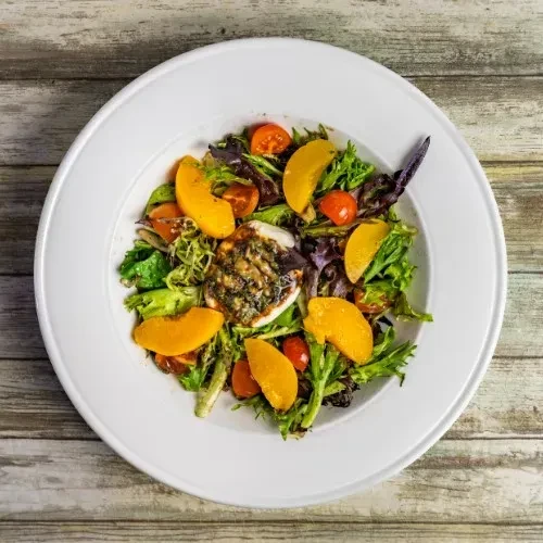 Overhead shot of a fresh salad with fruit, greens, and cheese.